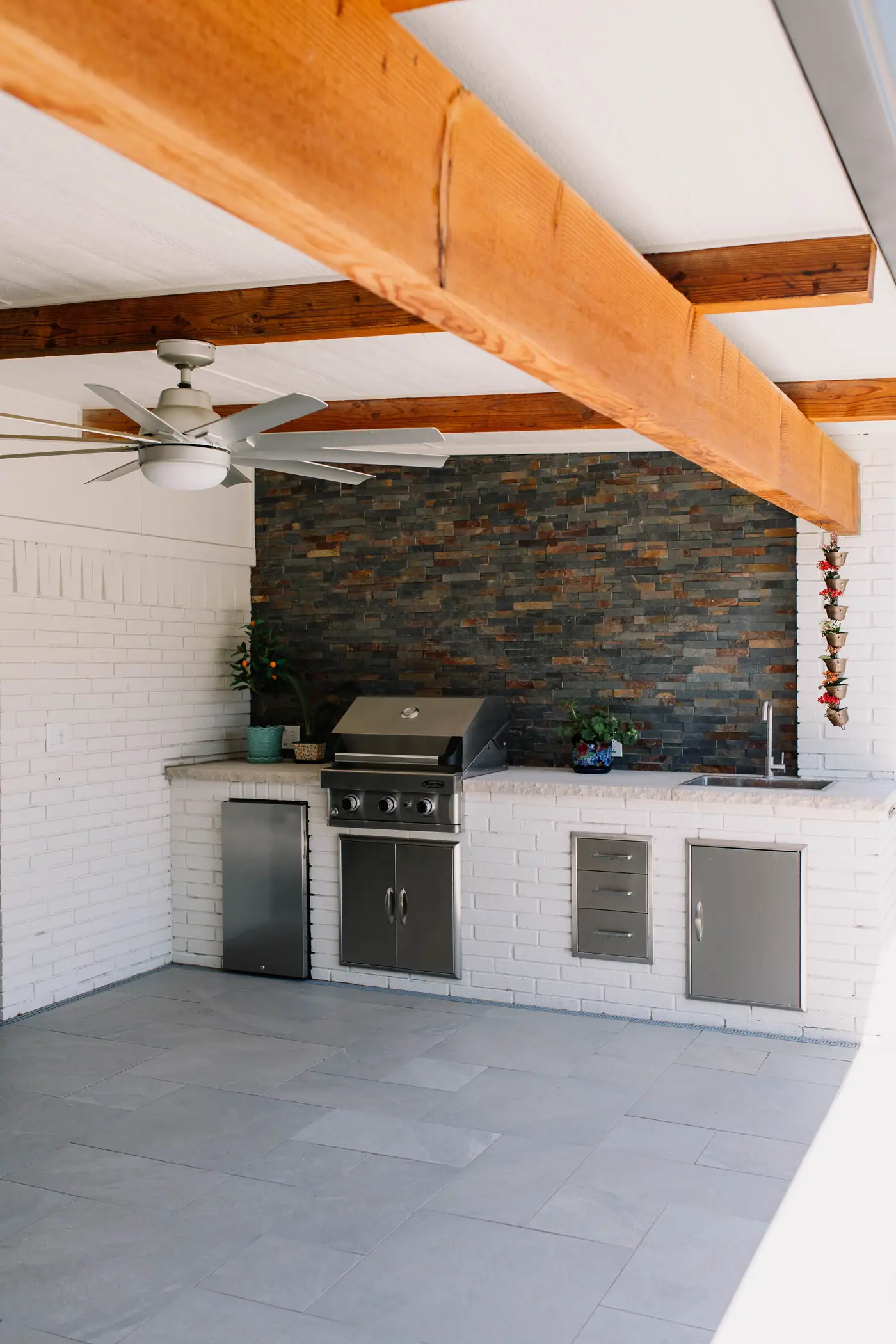 The Wedgwood outdoor kitchen from its open end: a cedar beam and ceiling fan overhead, the counter run and slate wall below