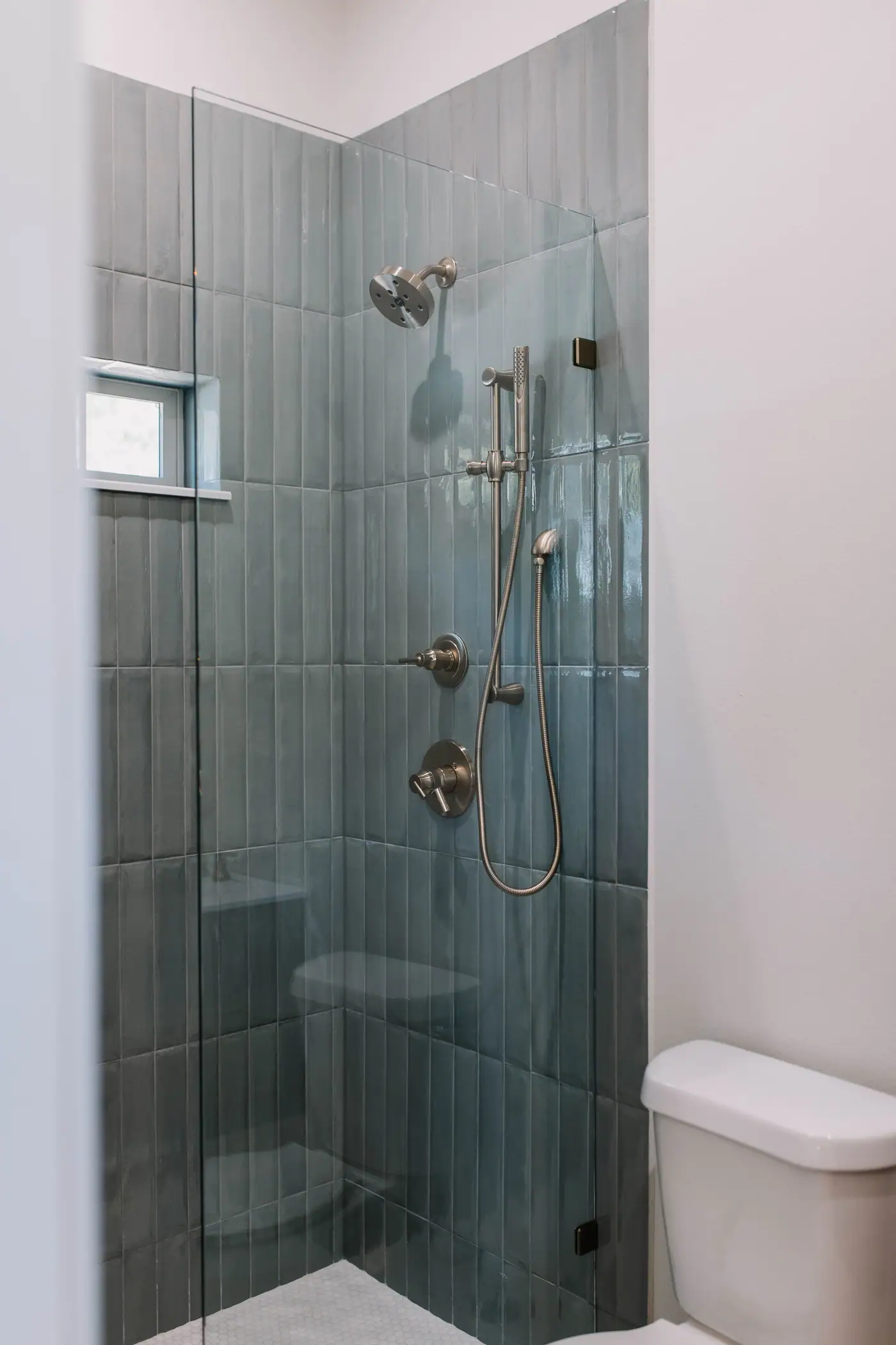 Walk-in glass shower with blue-green vertical tile and a handheld shower in the bath of an Arlington Heights backyard casita by 6th Ave Homes