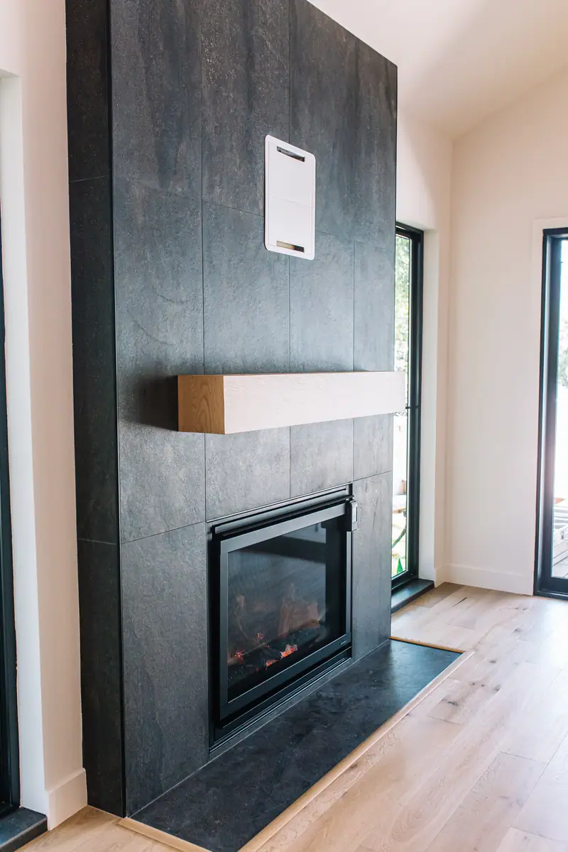 Floor-to-ceiling charcoal limestone-look tile fireplace with a white oak mantel