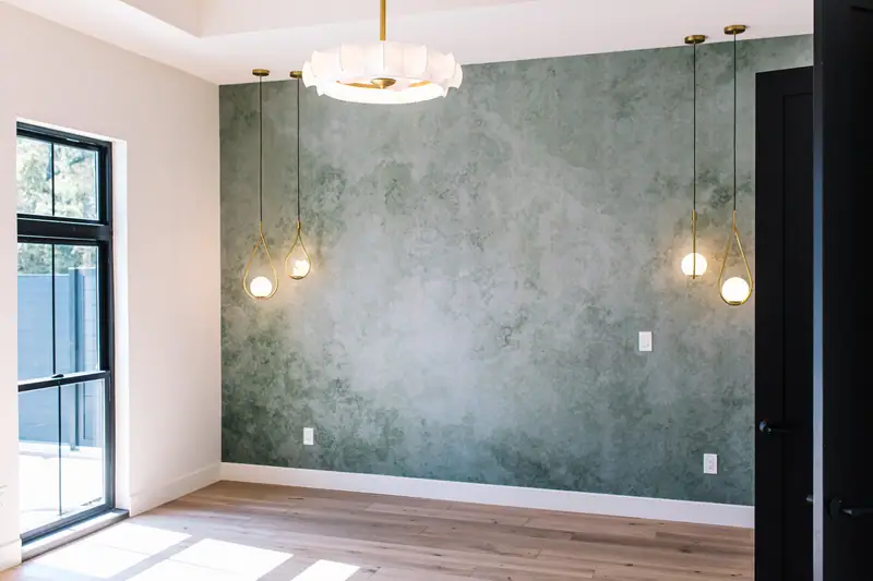 Primary bedroom with the light green plaster-look wallpaper accent wall, brass pendants and black window frames