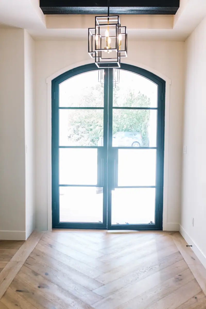 Arched black entry doors under a lantern, opening onto engineered white oak flooring
