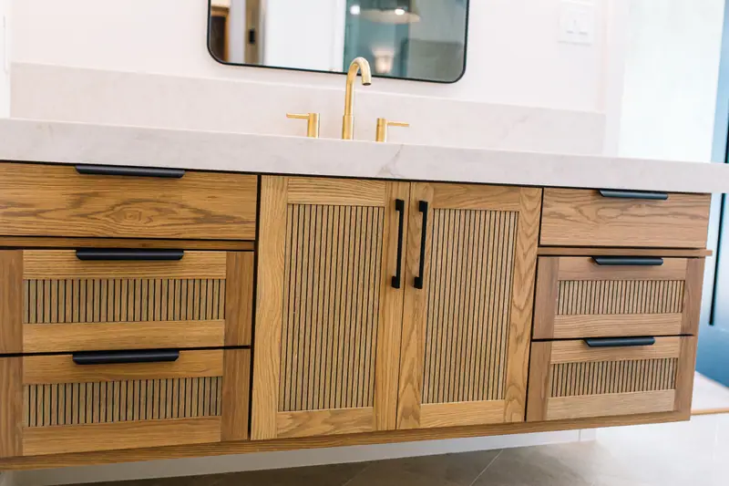 Fluted white oak vanity with a quartz counter, a brass tap and black hardware