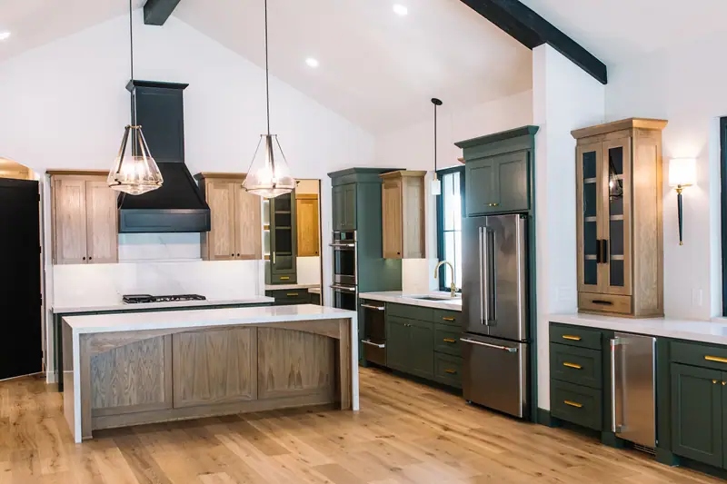 Kitchen with a white oak island, black range hood, sage green cabinetry and glass-front white oak cabinets under the cathedral ceiling