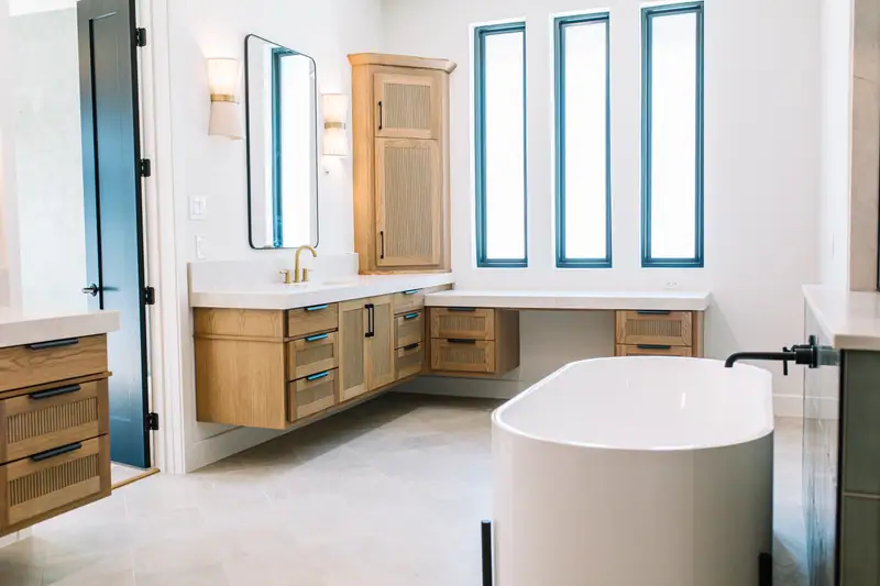 Primary bathroom with a centered soaking tub, white oak cabinetry and a run of tall windows