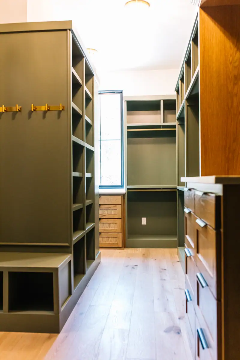 Walk-in closet fitted out in sage green shelving with white oak drawers and a quartz-topped island