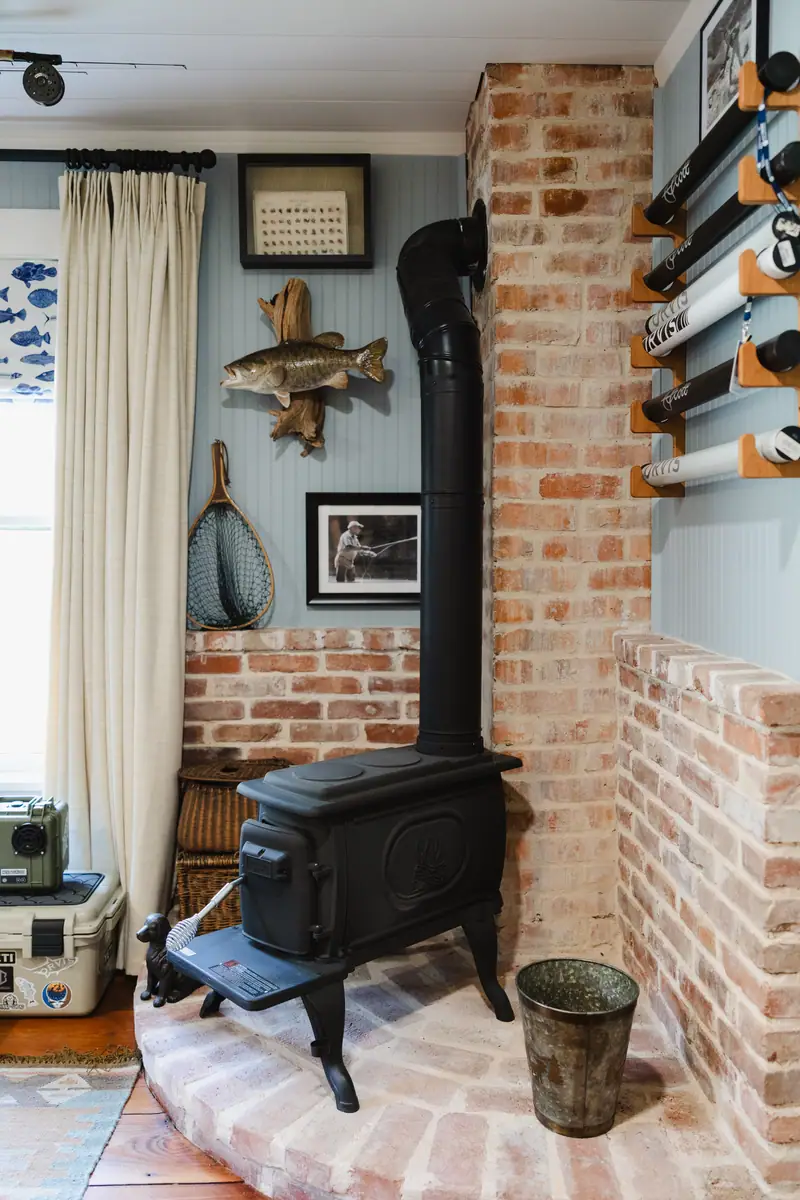 Tiny wood-burning fireplace set into the restored brick flue, with wall-mounted rod storage beside it