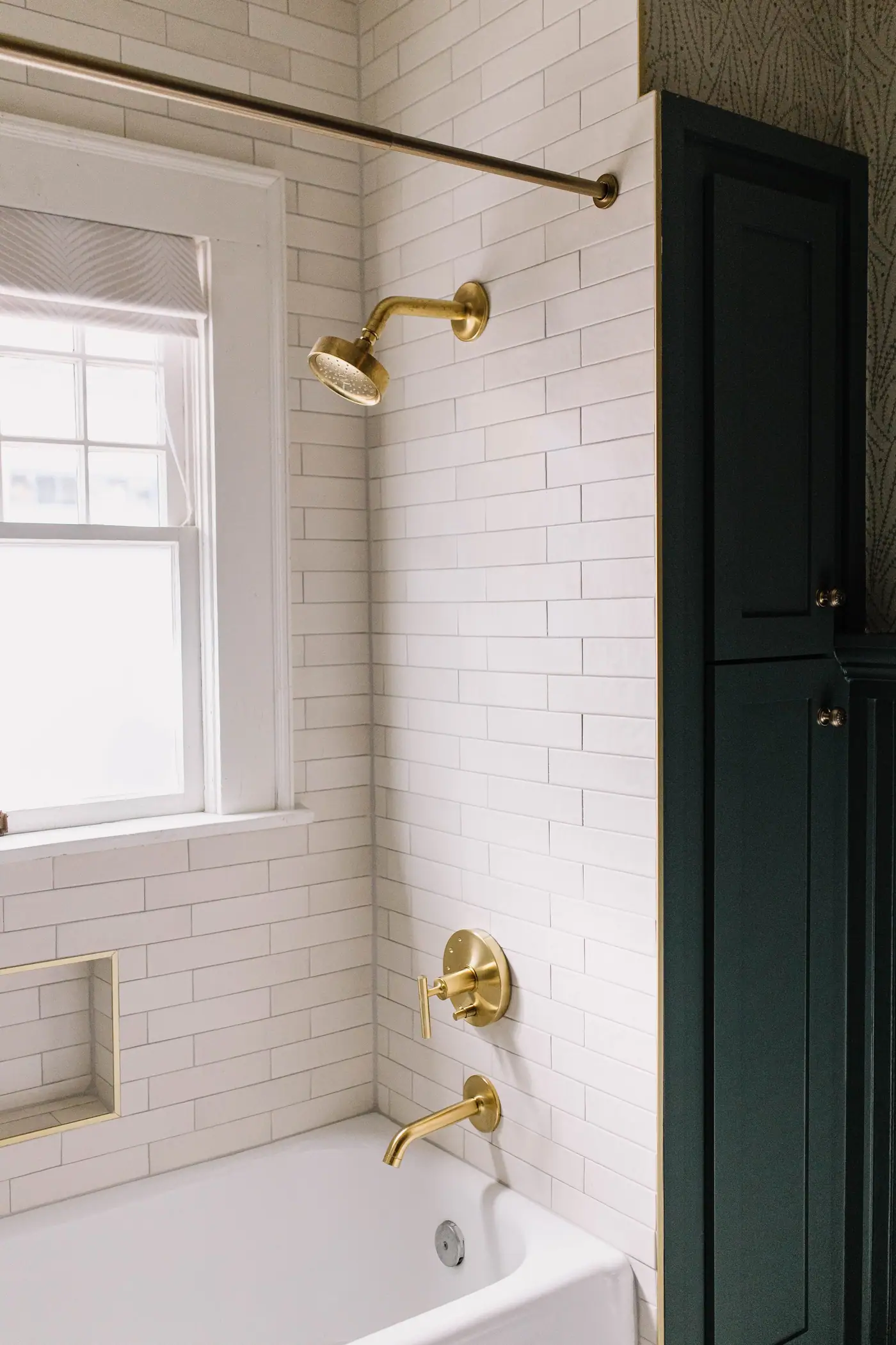 A hall bathroom with its original cast-iron tub, a white subway surround, a brass curtain rod and a brass showerhead.