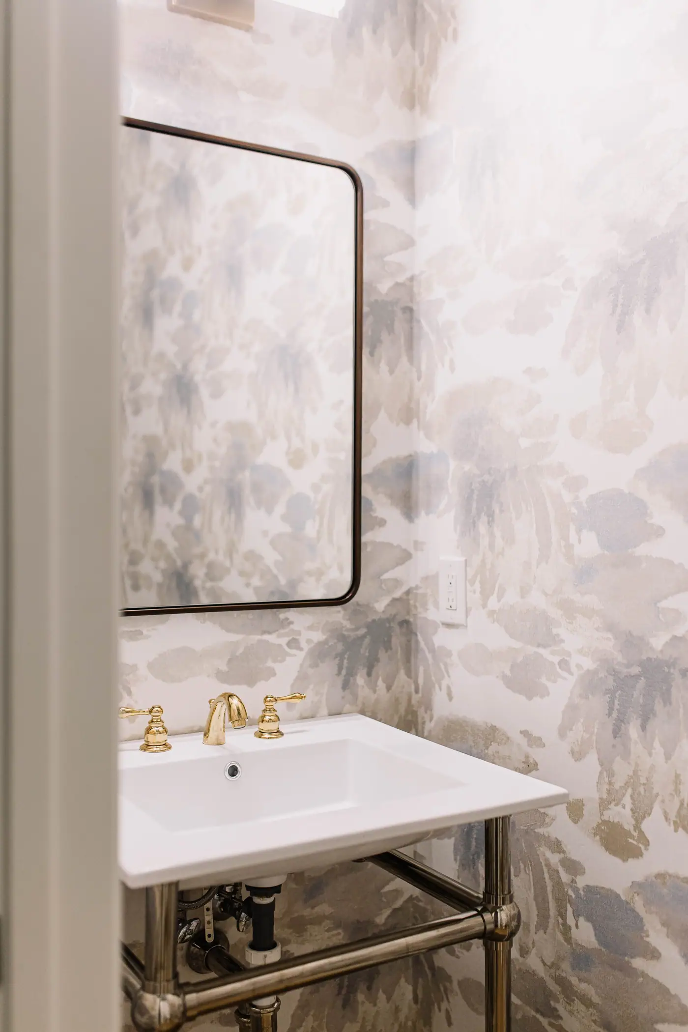 A powder room in a Mira Vista house, with watercolor botanical wallpaper and a brass-legged console basin.