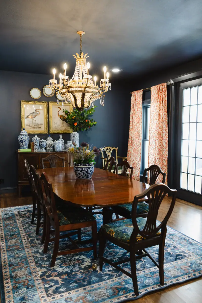 Dining room drenched in navy on the walls and ceiling, with a brass chandelier, an antique table and chairs and a blue patterned rug