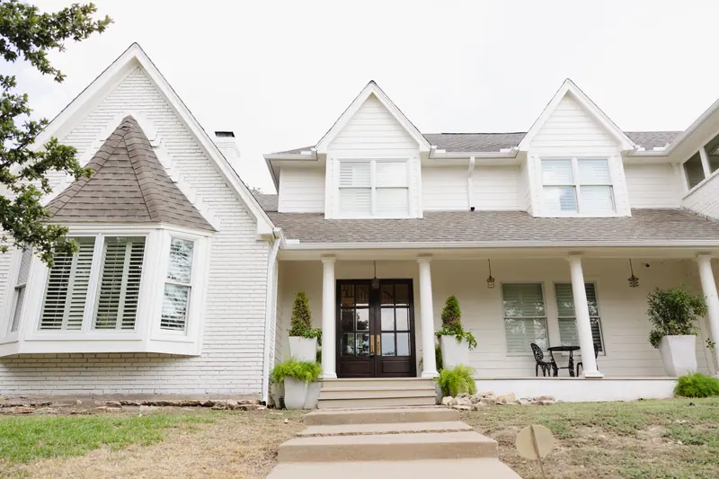 Front elevation of a Mont Del home in Fort Worth with painted white brick and lap siding, twin gabled dormers, a columned porch and dark wood double entry doors