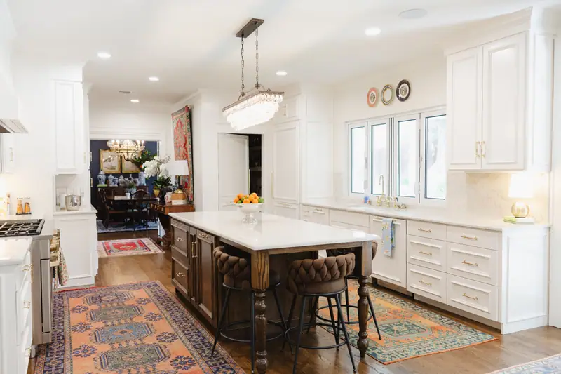 Kitchen with white inset cabinetry and brass hardware, a dark wood island with turned legs and tufted leather stools, opening to the navy dining room