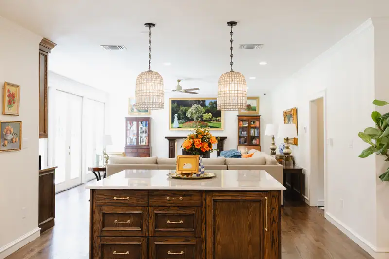 Second kitchen island in dark oak with woven pendants above, open to the family room and its painted fireplace beyond