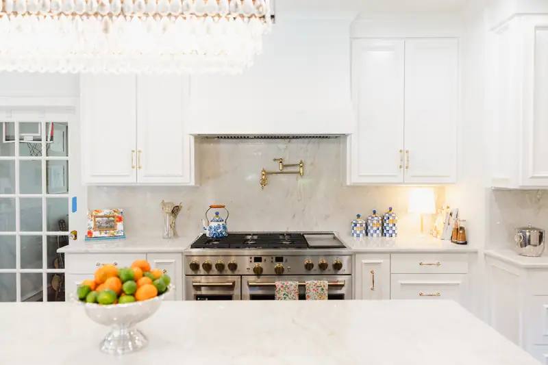 Kitchen range wall with Taj Mahal countertops and a full-height stone backsplash, a brass pot filler and a professional range