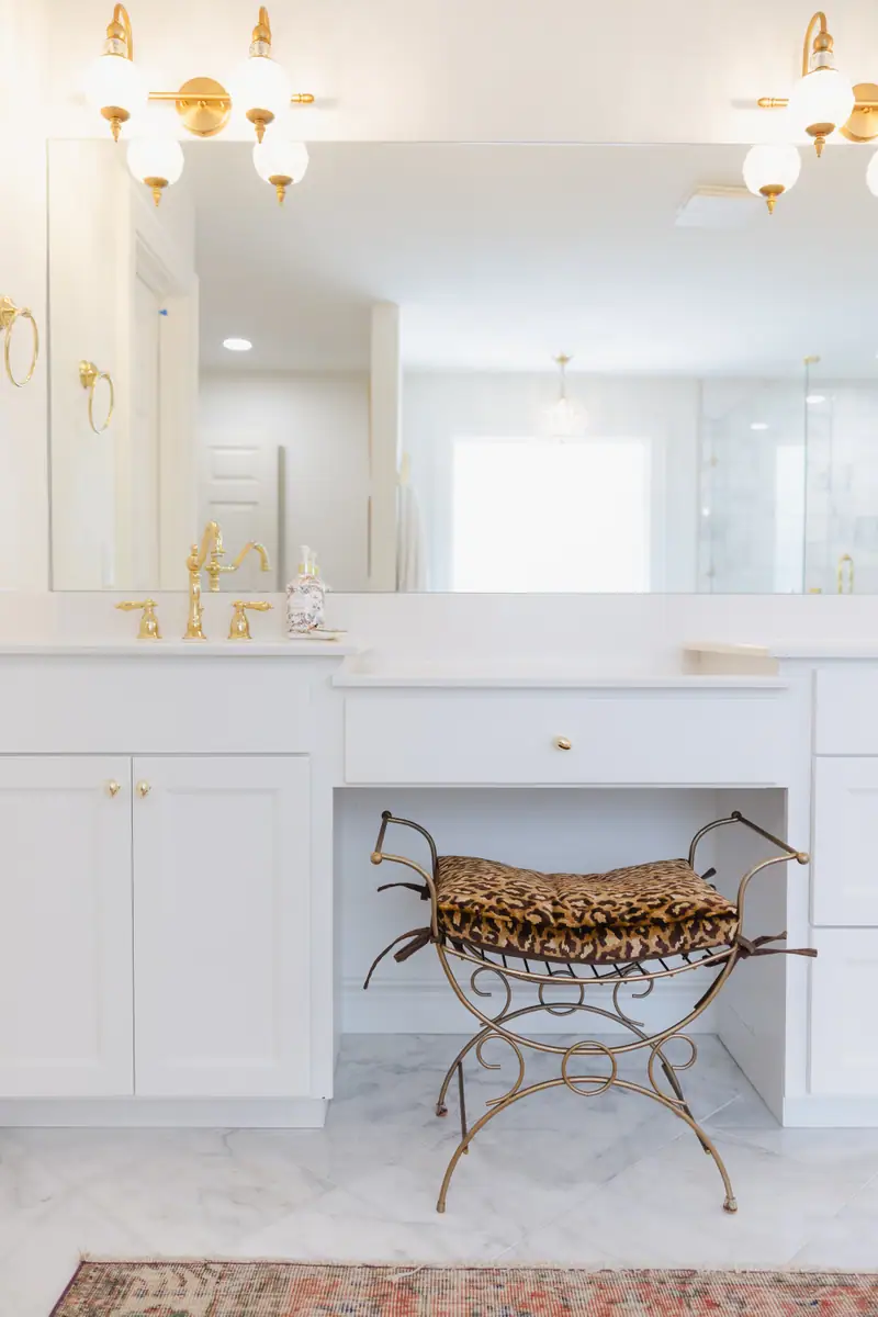 Primary bathroom vanity with a marble floor, brass sconces, polished brass faucet and a full-width mirror