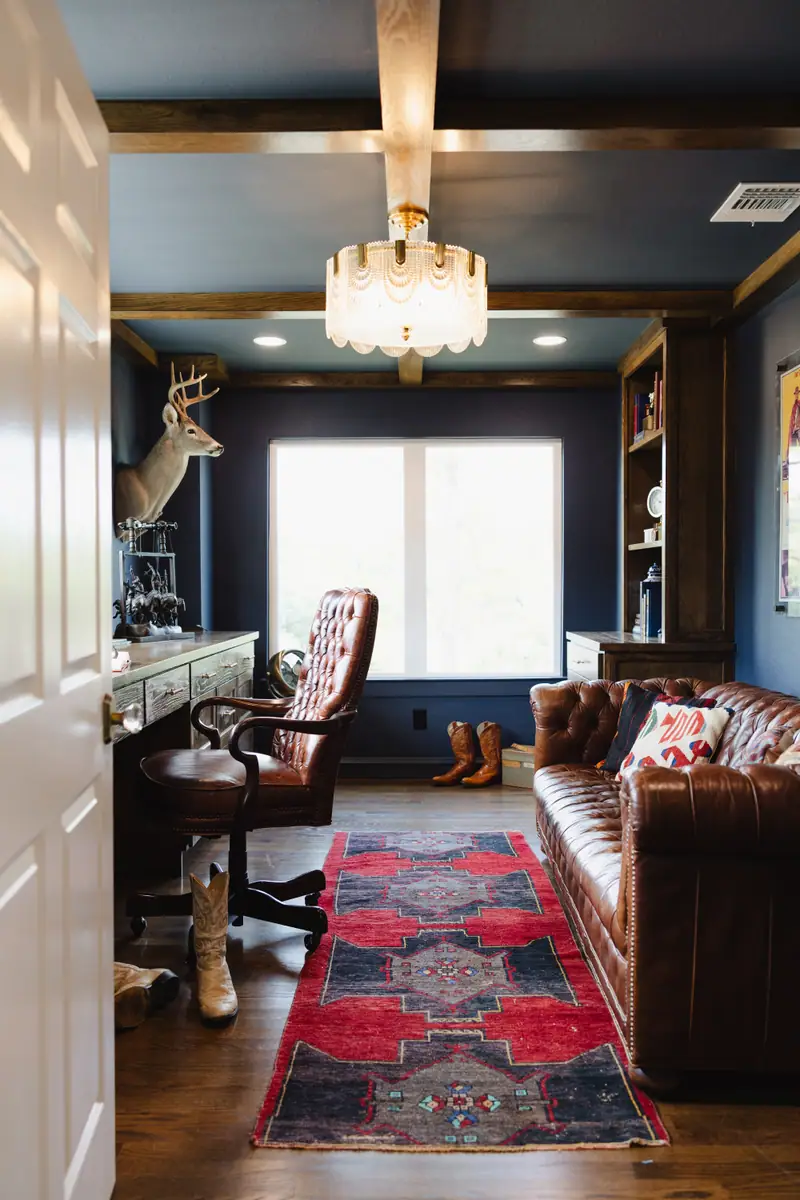 Study with navy walls, stained wood ceiling beams, a built-in desk, bookcases and a leather chesterfield sofa