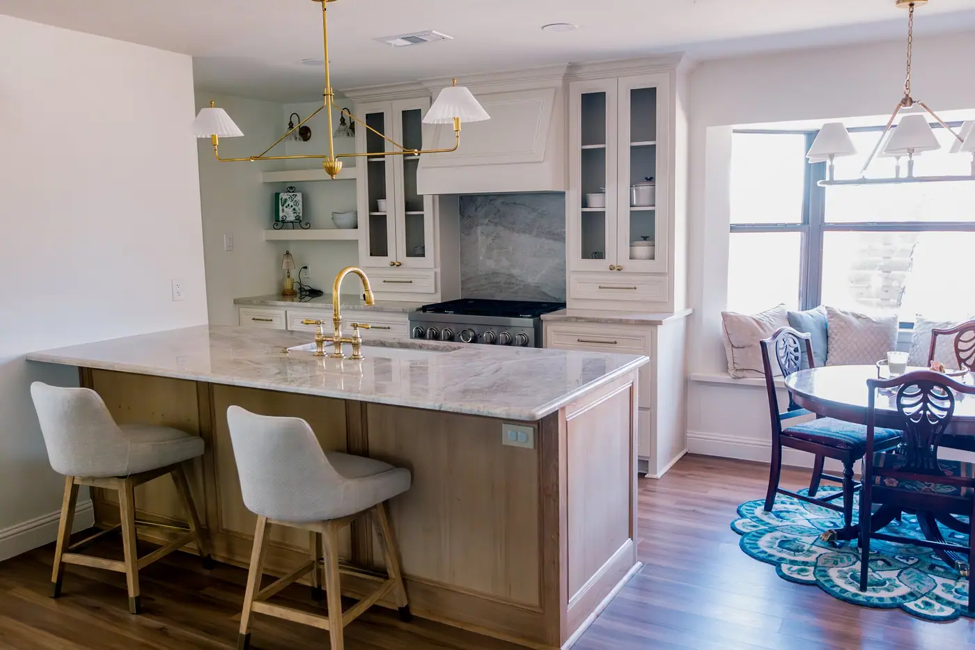A bright kitchen with a white marble waterfall island, limed-oak cabinetry and a brass bridge faucet
