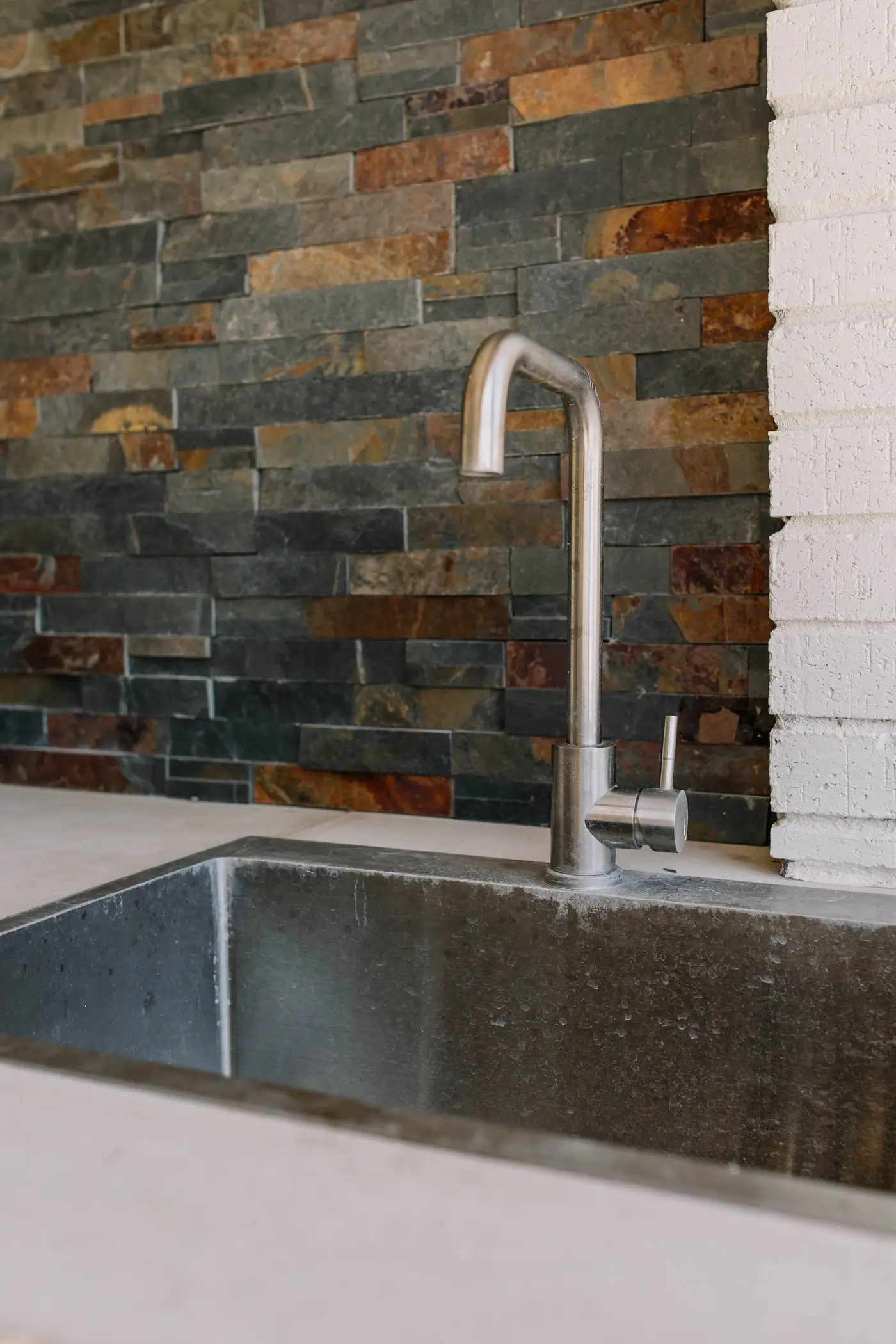 Close on the Overton Park outdoor kitchen sink: a stainless basin and tall faucet set against the slate backsplash