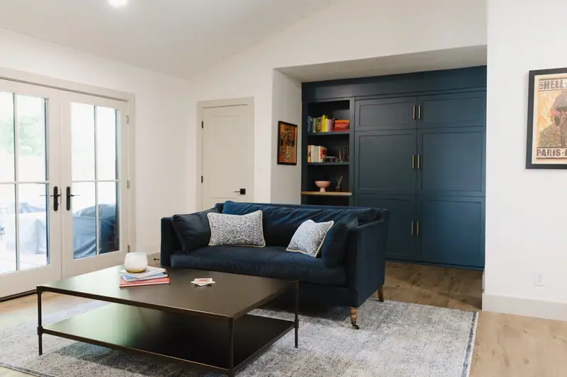 Den with floor-to-ceiling navy built-in cabinetry, a navy velvet sofa and French doors to the yard