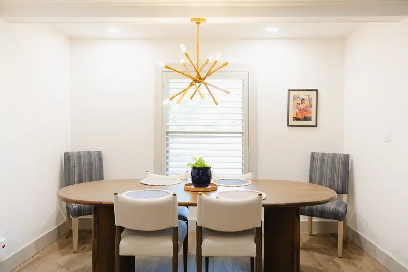 Dining room with an oval wood table, striped blue side chairs and a brass sputnik chandelier
