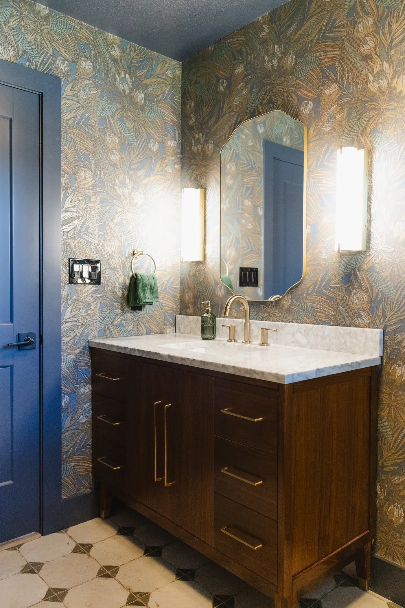 Half bath wrapped in moody blue and gold botanical wallpaper, with a dark wood vanity and a checkerboard tile floor