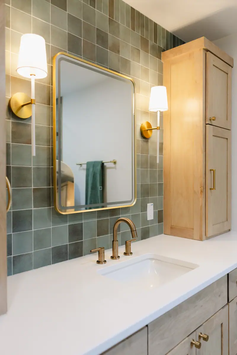 Jack-and-Jill bathroom with green square tile, a light wood vanity and an arched brass mirror