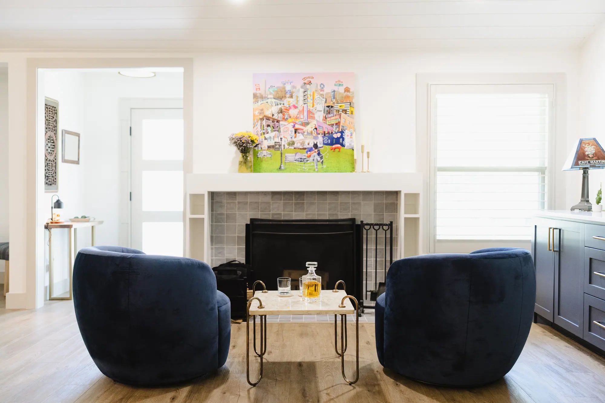 Living room with a tiled fireplace, two navy velvet swivel chairs and a brass-framed stone table