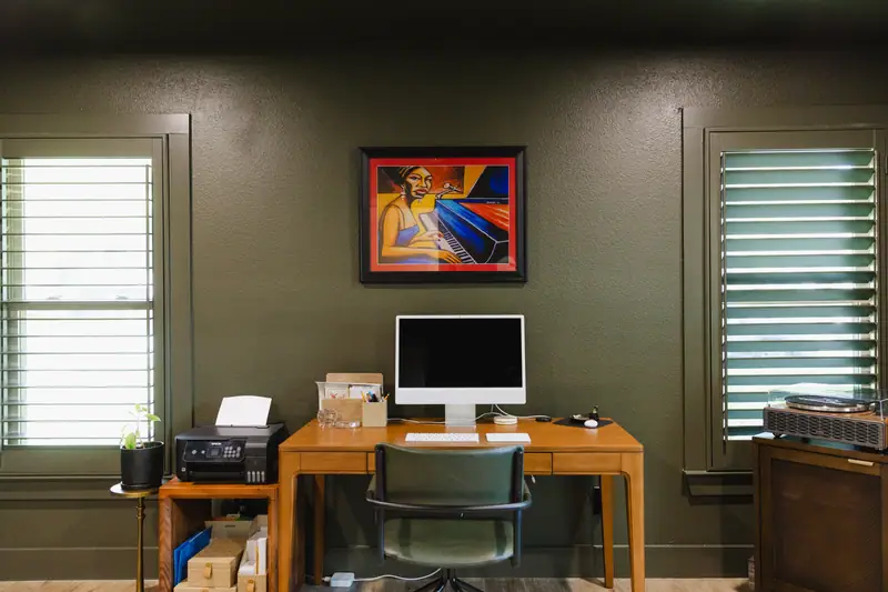 Home office painted deep green, with plantation shutters, a wood desk and a record player