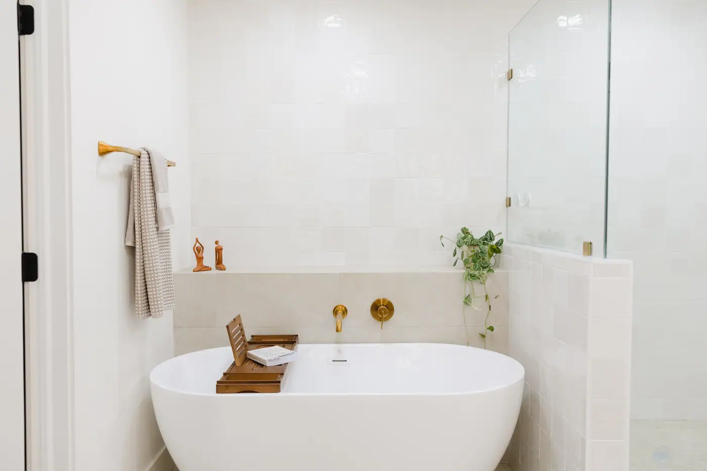 Freestanding soaking tub with a brass wall-mount filler against square white tile