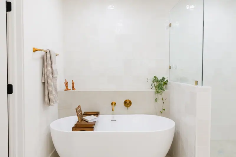 Freestanding soaking tub with a brass wall-mount filler against square white tile