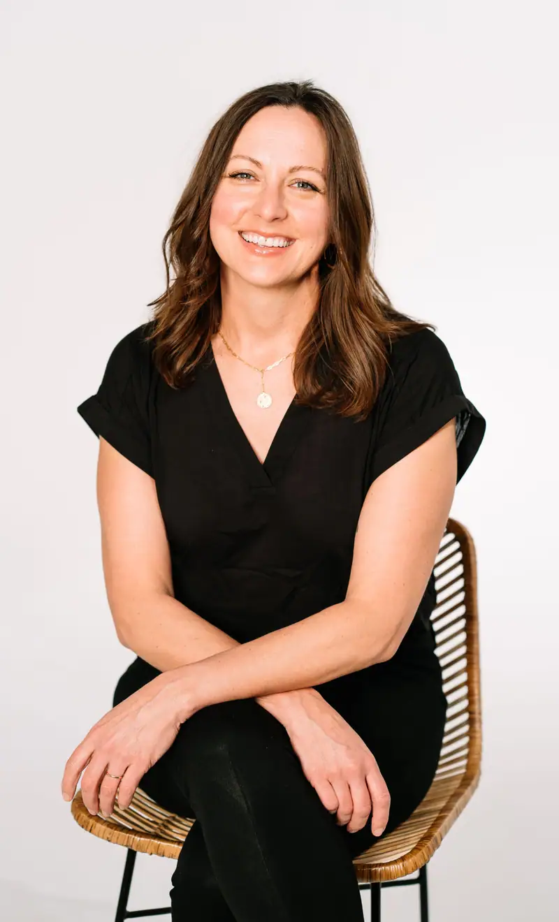 Joanna Batsel seated on a rattan chair against a white wall