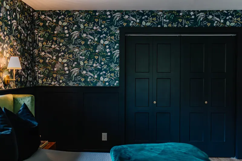 A Fort Worth primary suite with dark botanical wallpaper, navy wainscot, black closet doors, and a teal velvet bed