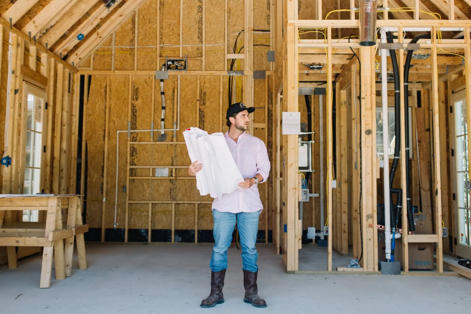 A 6th Ave Homes builder with rolled plans inside the wood framing and rough-in of a Fort Worth whole-home renovation