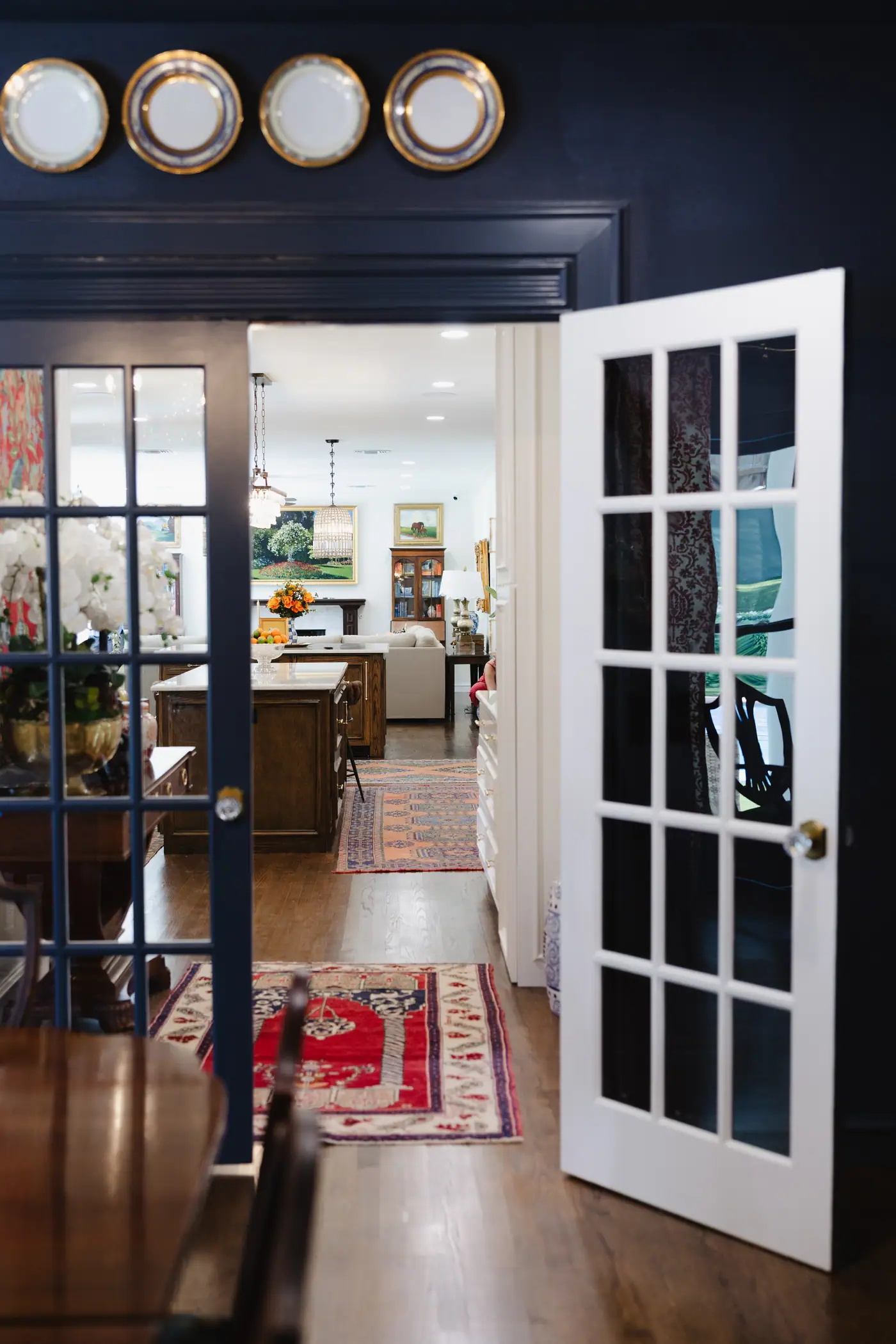 French doors open from a navy Fort Worth dining room onto one long sightline through the kitchen to the living room
