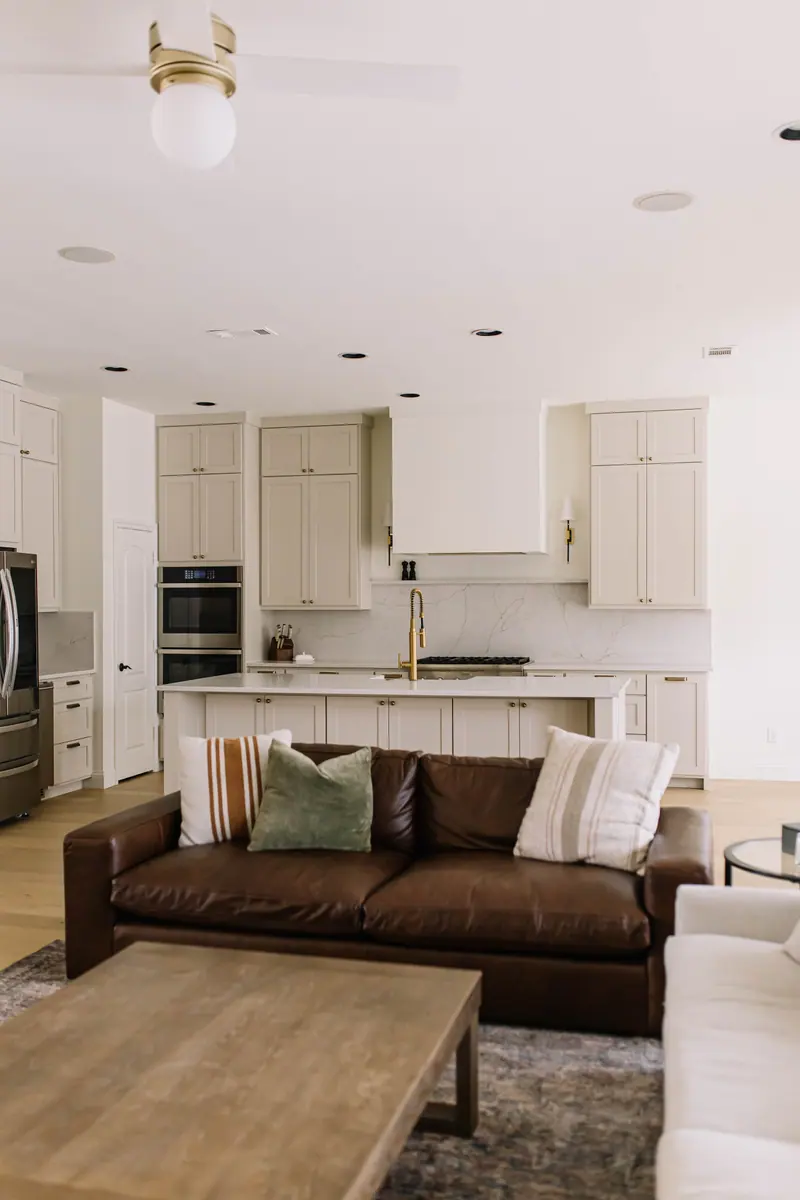 An opened Fort Worth floor plan after a whole-home remodel: a leather sofa in the great room with a clear sightline across to the kitchen island and range wall