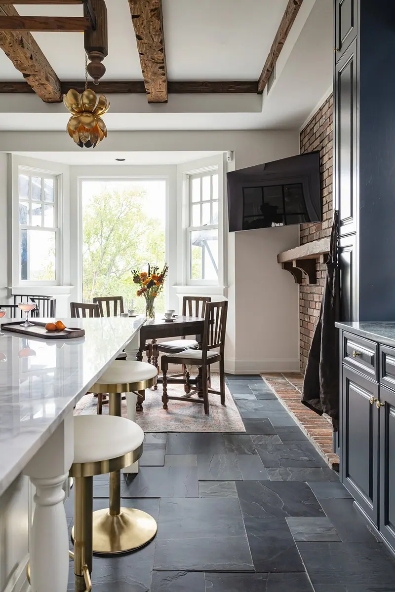 A Fort Worth whole-home remodel opened into one long room, with a marble island running past a bay-window dining area to an exposed-brick chimney under hewn beams