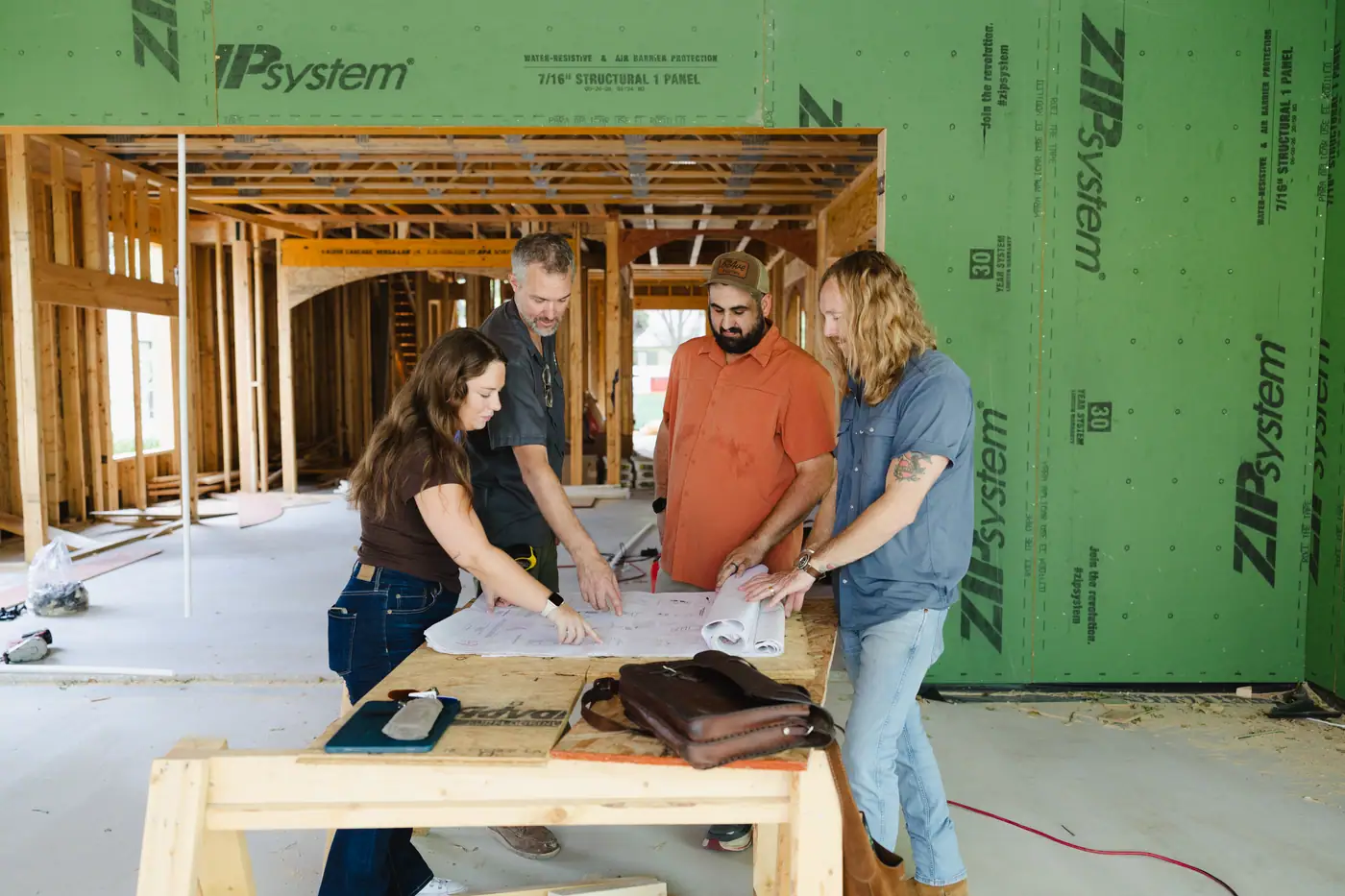 Four 6th Ave Homes team members reading a plan set together on a sawhorse table inside a framed Fort Worth home
